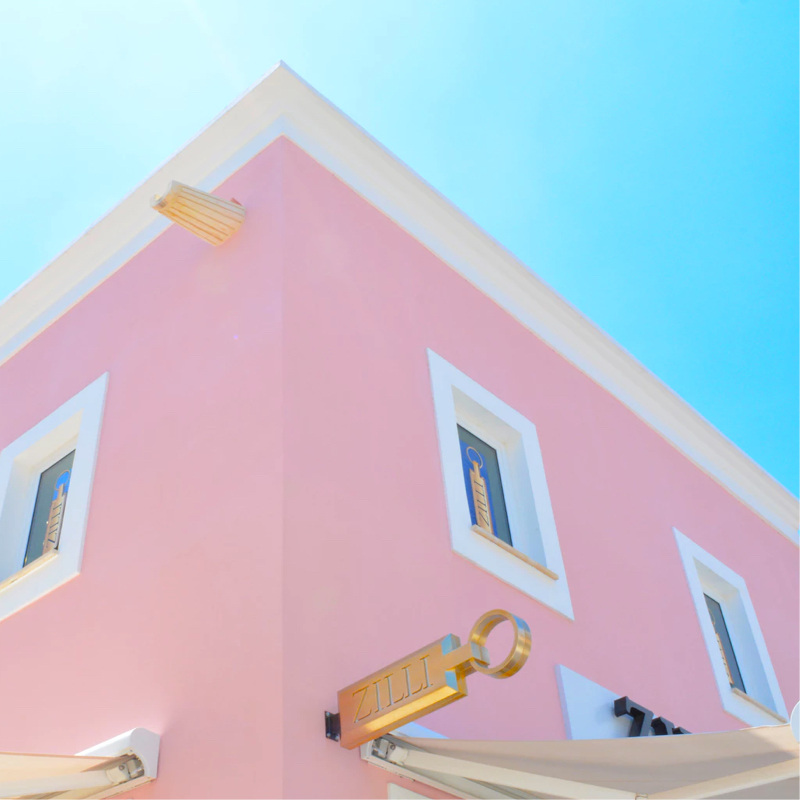 The corner of a pink building with white trim and gold accents. It has a gold sign that reads Zilli and appears to be a high-end storefront.