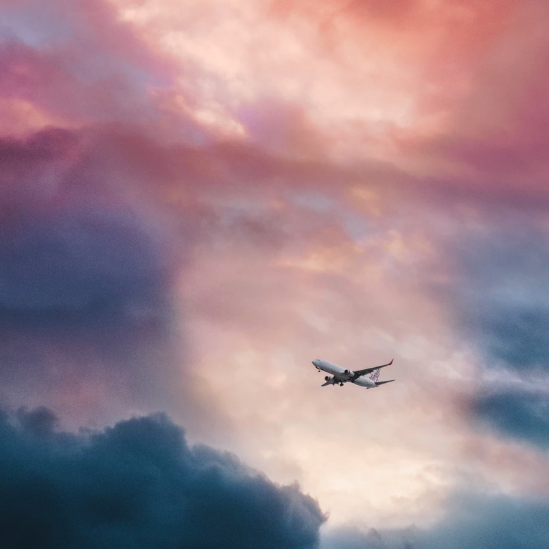 A passenger jet soaring through a dramatically cloudly sky. The sky is rich with pinks, ambres, and teals.